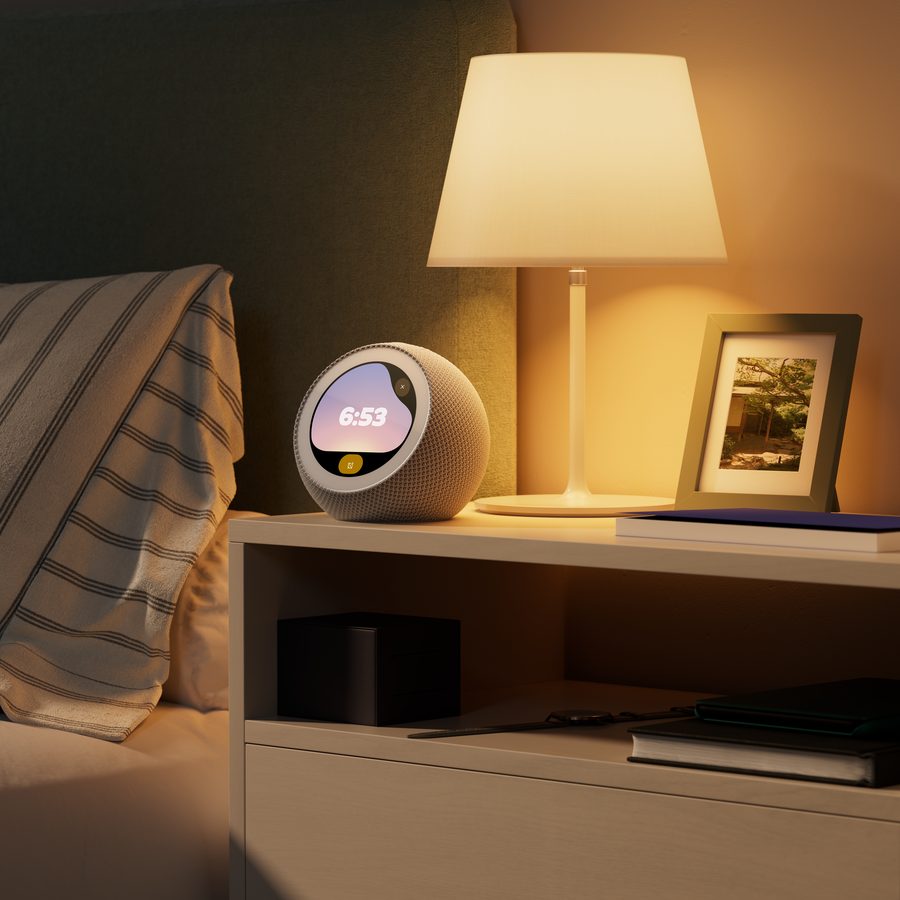 Despertador Amazon Echo Time con pantalla circular encendida sobre una mesilla de noche junto a una lámpara